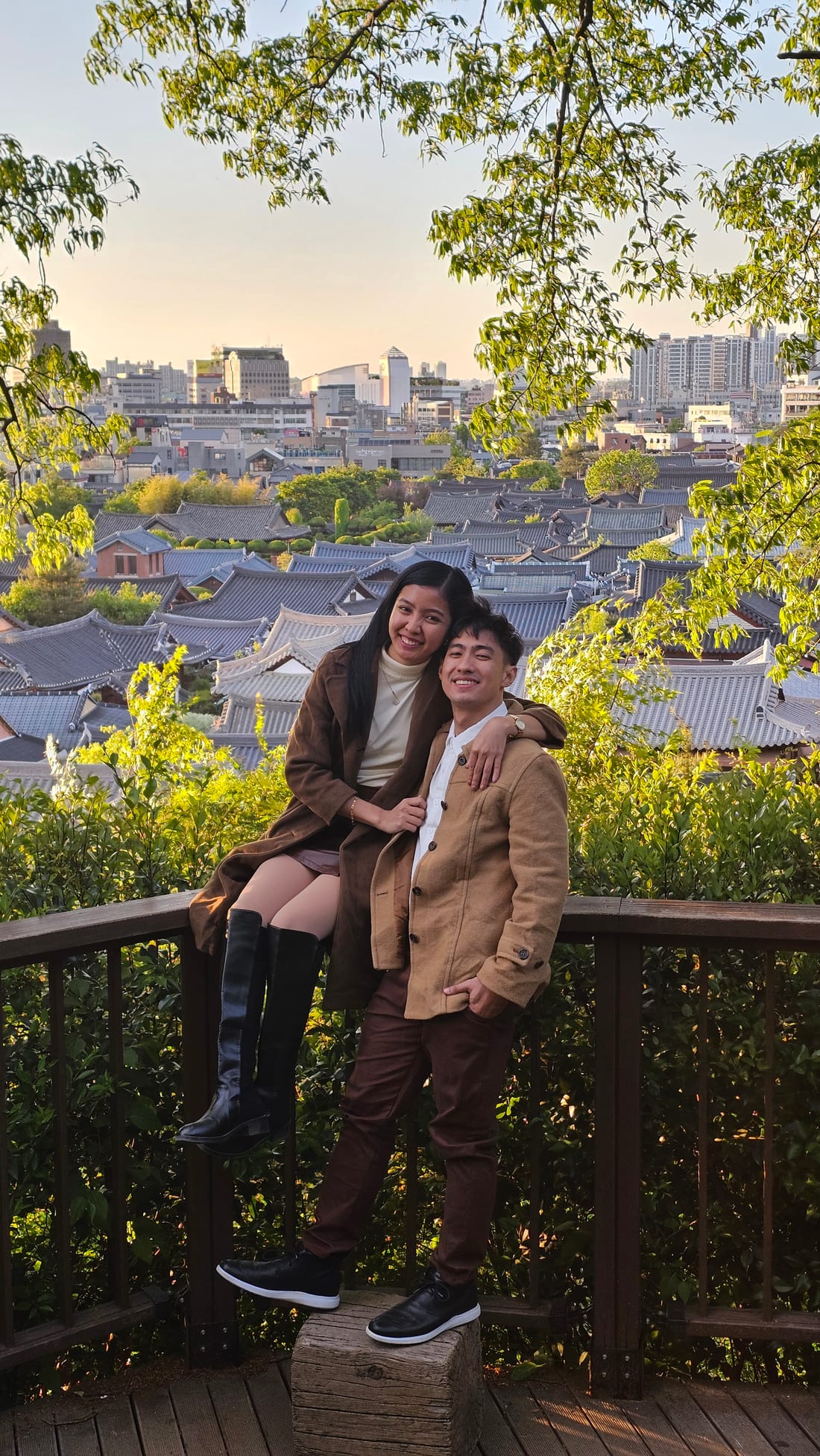 Jose and Rhoby on a railing above a Korean hanok village at sunset