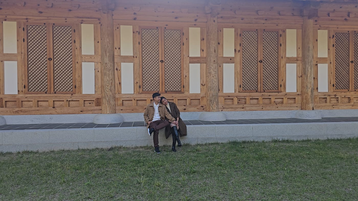 Jose and Rhoby sitting together on the stone step of a wooden hanok hall
